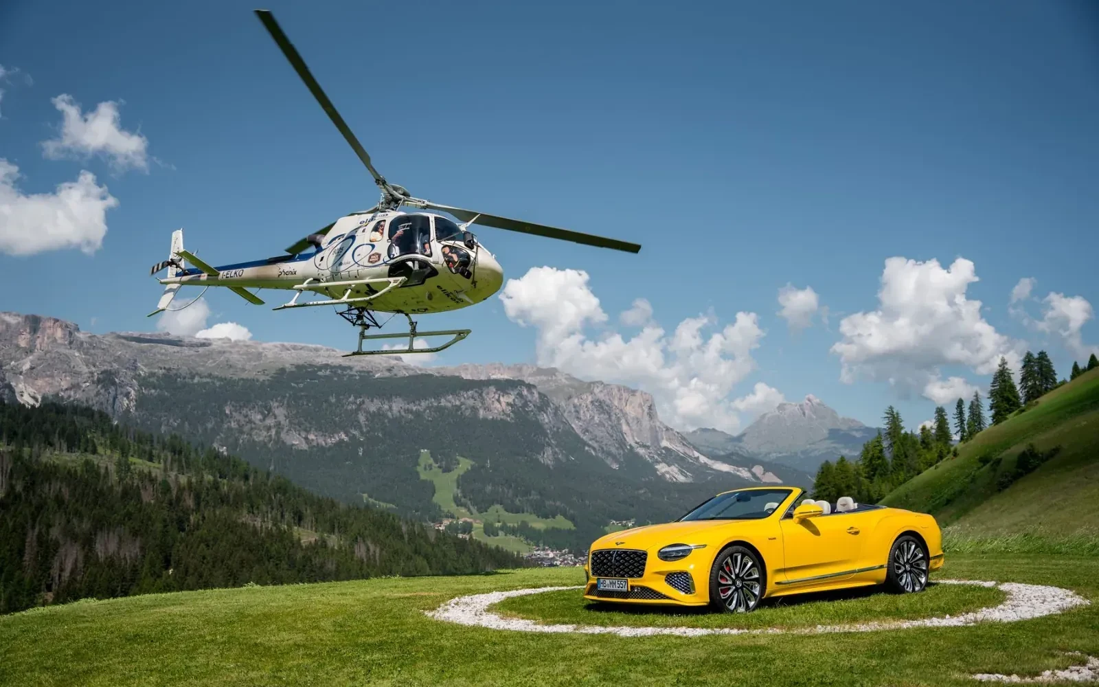Gelber Bentley Continental GTC und Hubschrauber über den Dolomiten