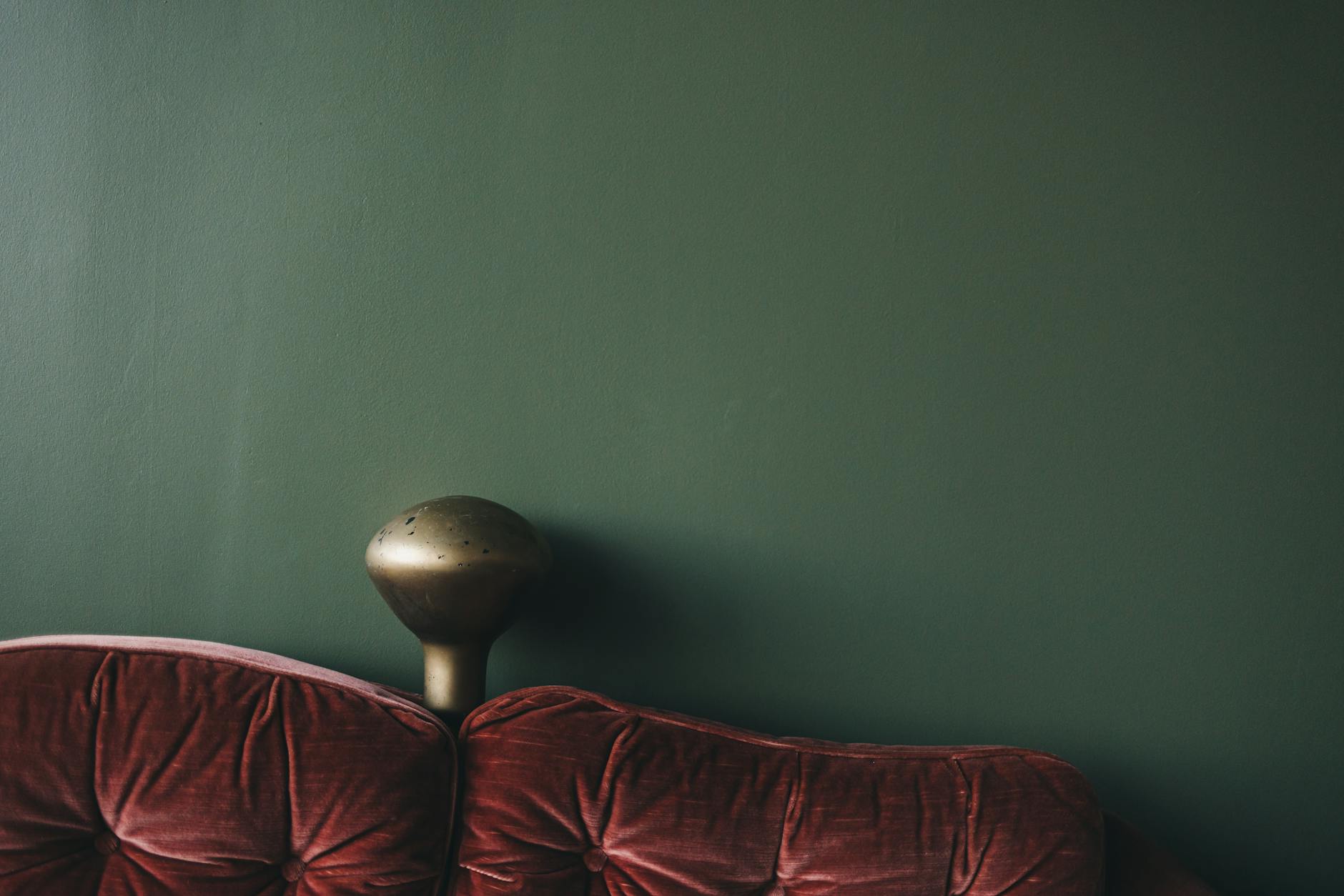 Rostroter Samtsofa vor moosgruener Wand mit Messinglampe, anti-minimalistisches Wohn-Setting im Geist von Gucci Decor