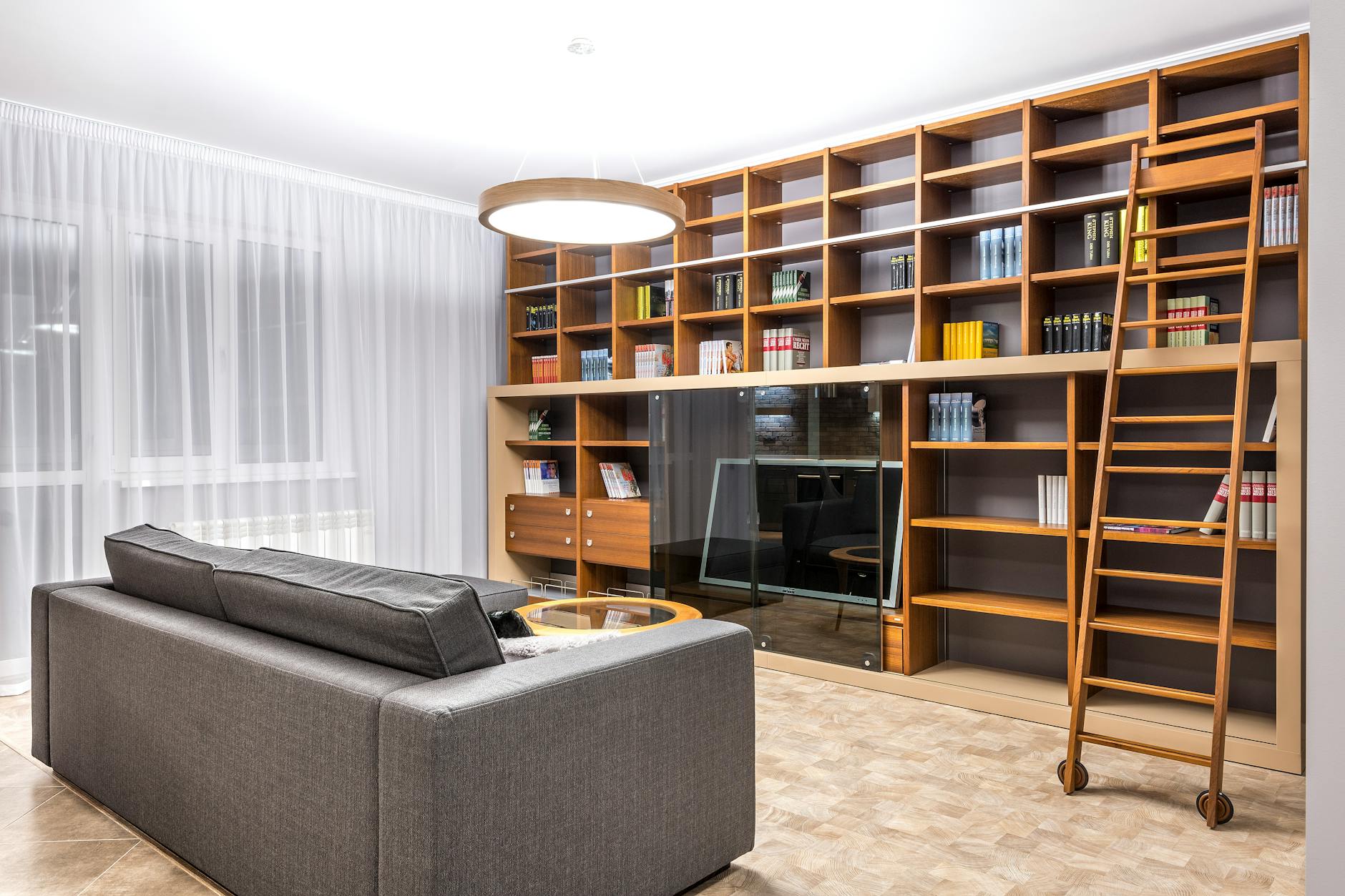 Wohnzimmer mit raumhoher Bücherwand aus Holz und einer Bibliotheksleiter