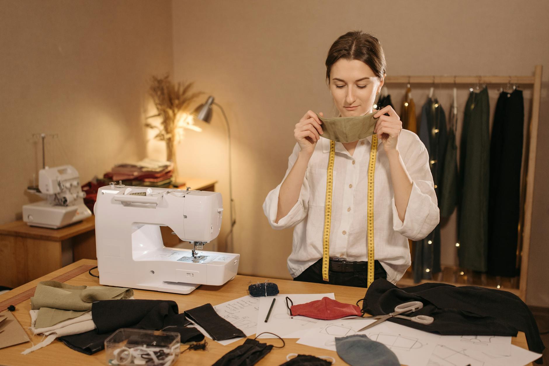 Seamstress in her studio checks a hand-sewn fabric mask, with sewing machine and fabrics beside her