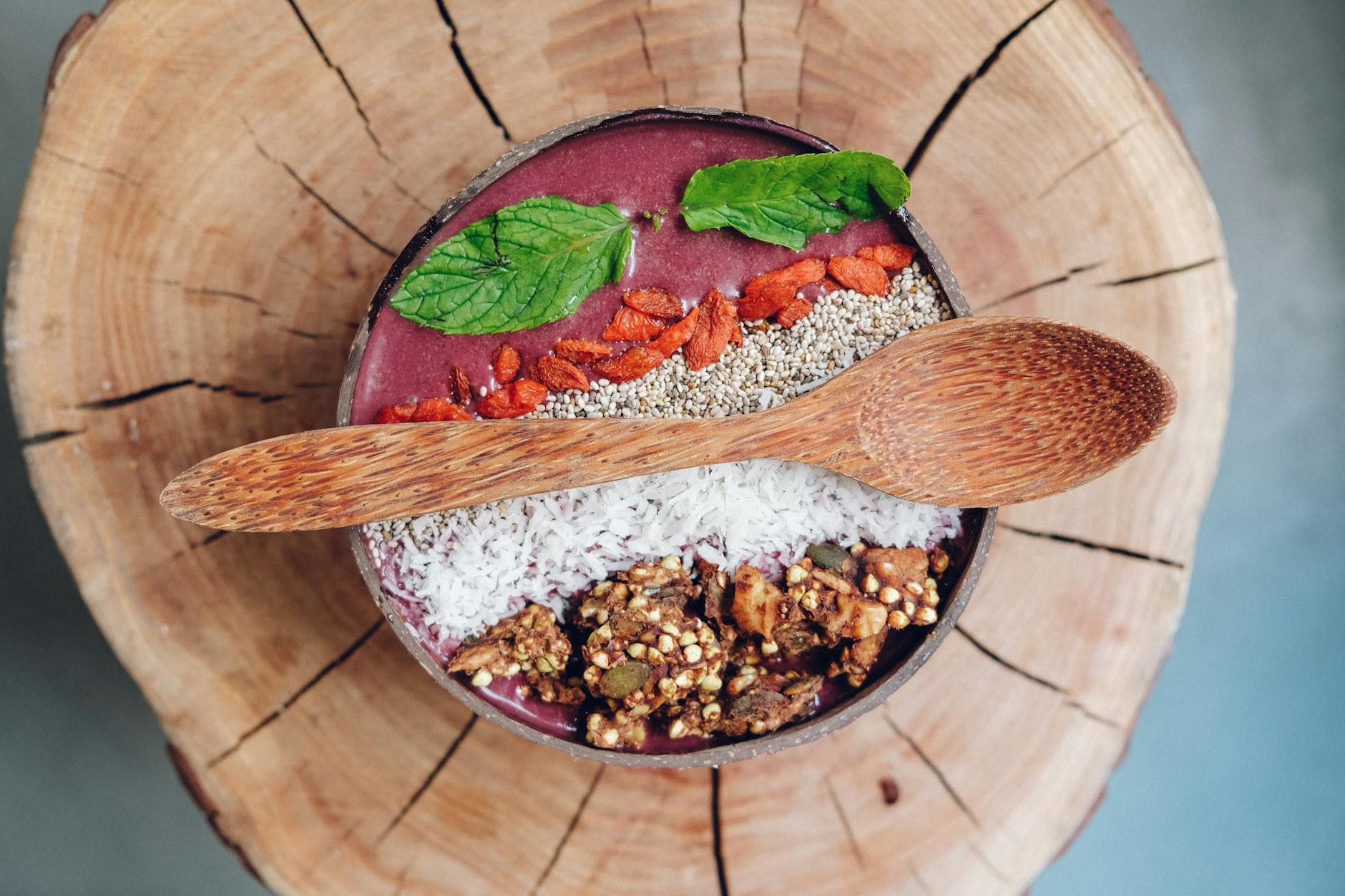 Acai bowl topped with fresh berries, granola and mint in a wooden bowl
