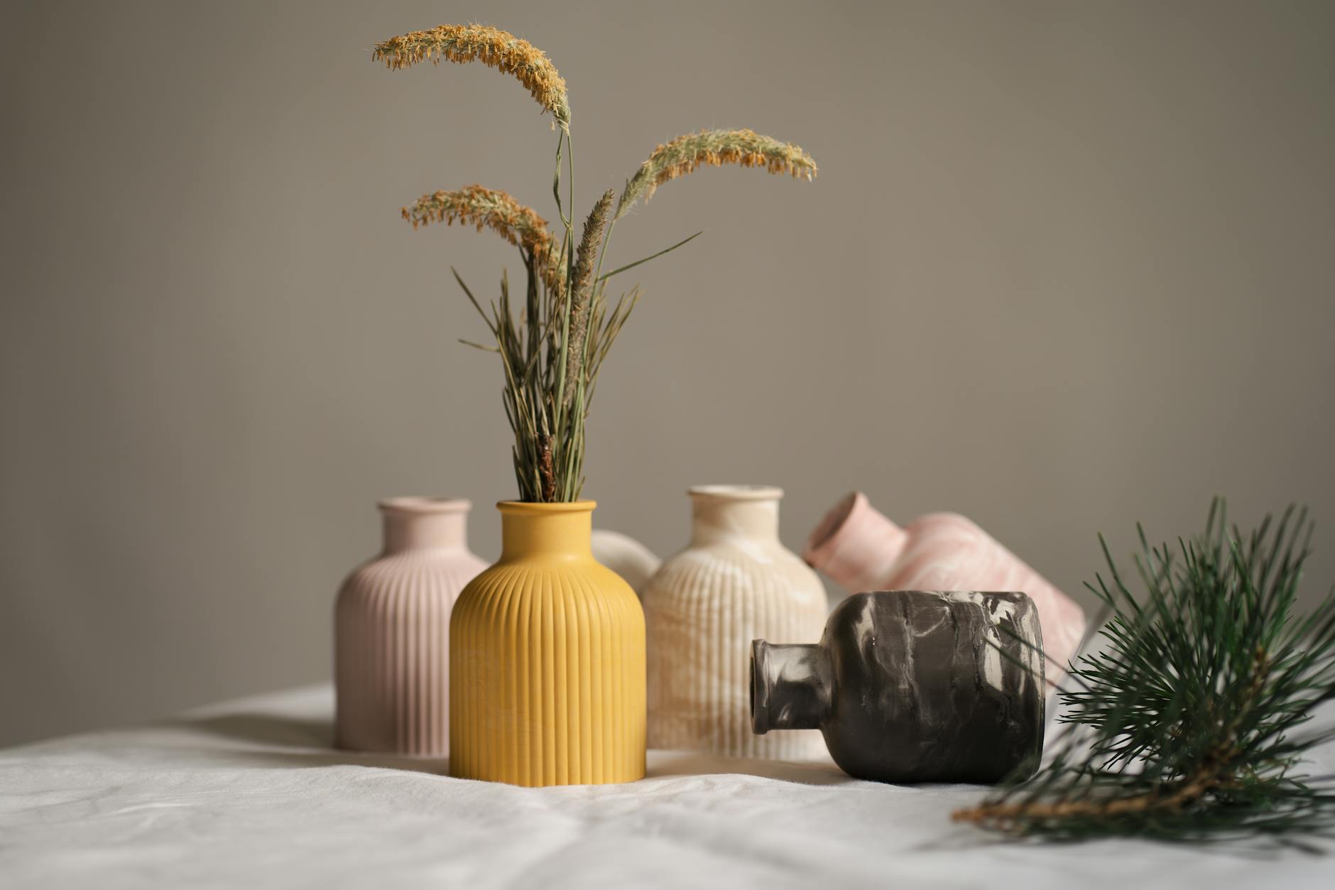 Several pastel ceramic vases with dried flowers arranged on a wooden table