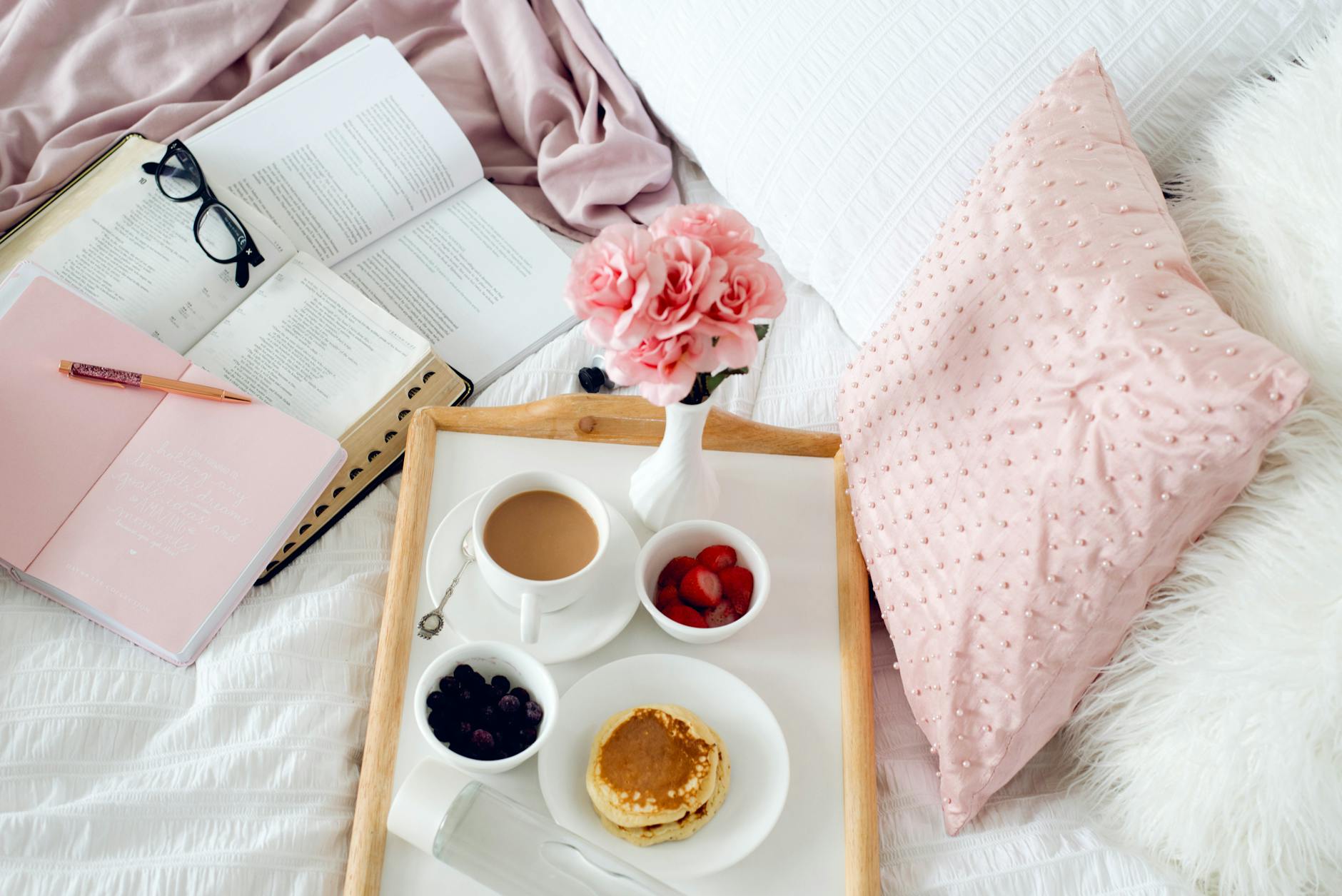 Valentinstag-Frühstück ans Bett: Tablett mit Kaffee, Pancakes, Beeren und frischen Blumen auf hellem Leinen