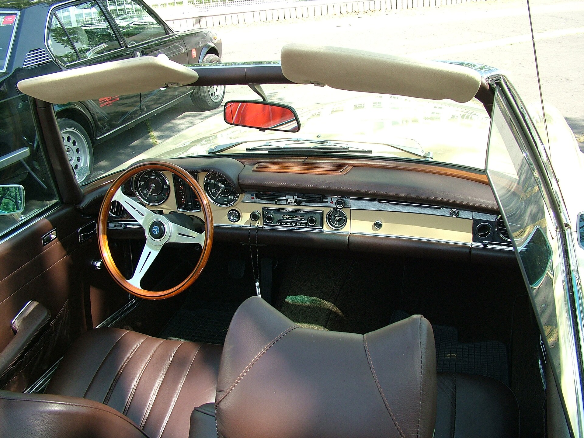 Interior of a Mercedes-Benz 280 SL W 113 with large wooden steering wheel, round dials and minimalist dashboard