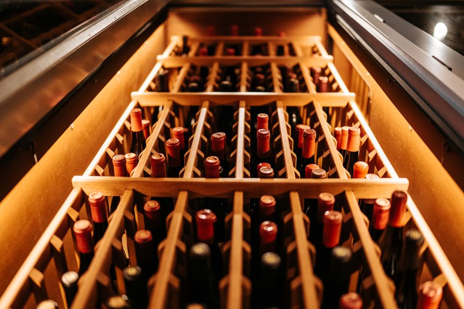 Wine bottles in warmly lit wooden shelving inside a wine cellar