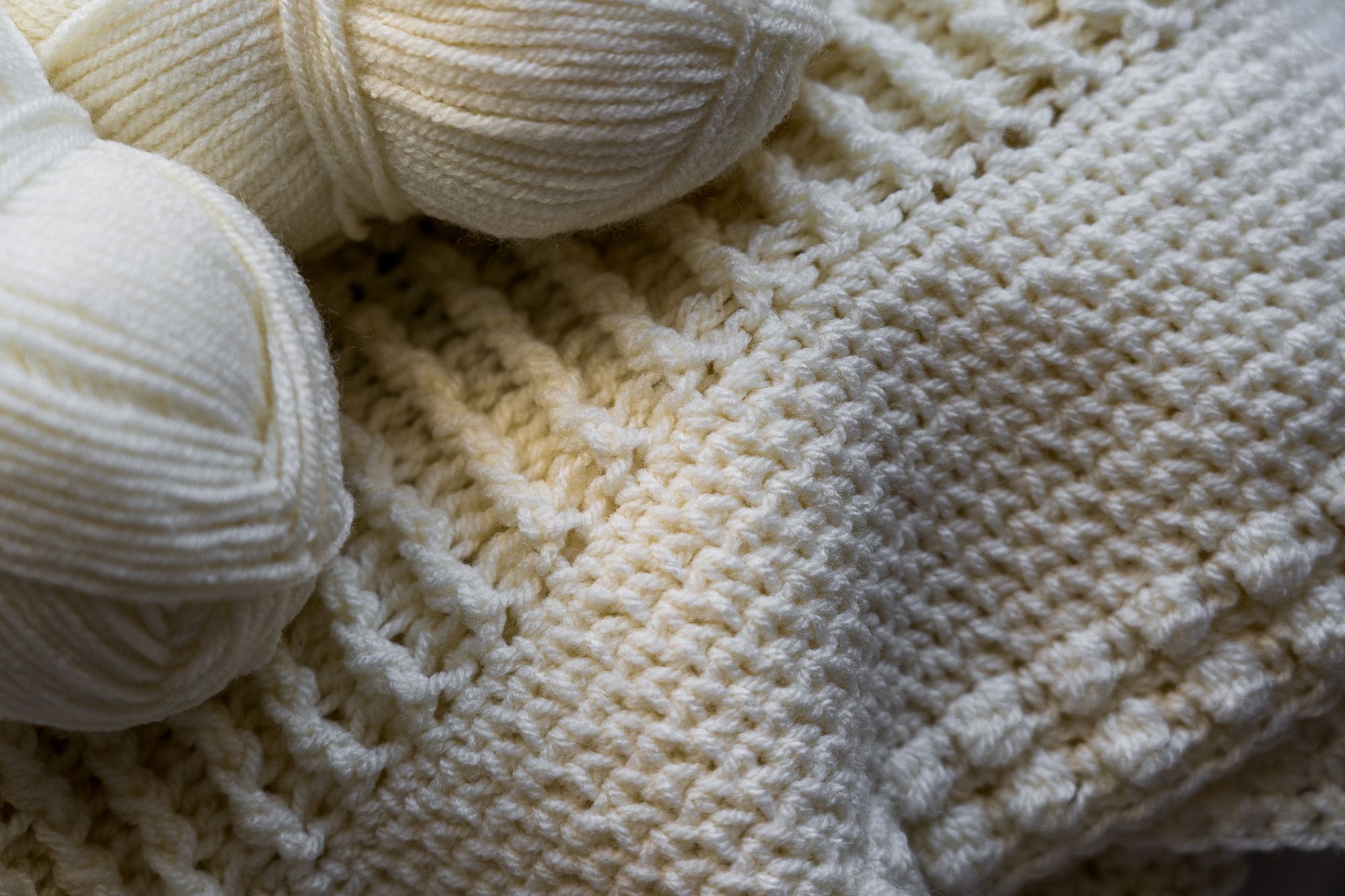 Cremefarbene Garnknäuel neben einer gestrickten Bahn mit deutlicher Maschenstruktur