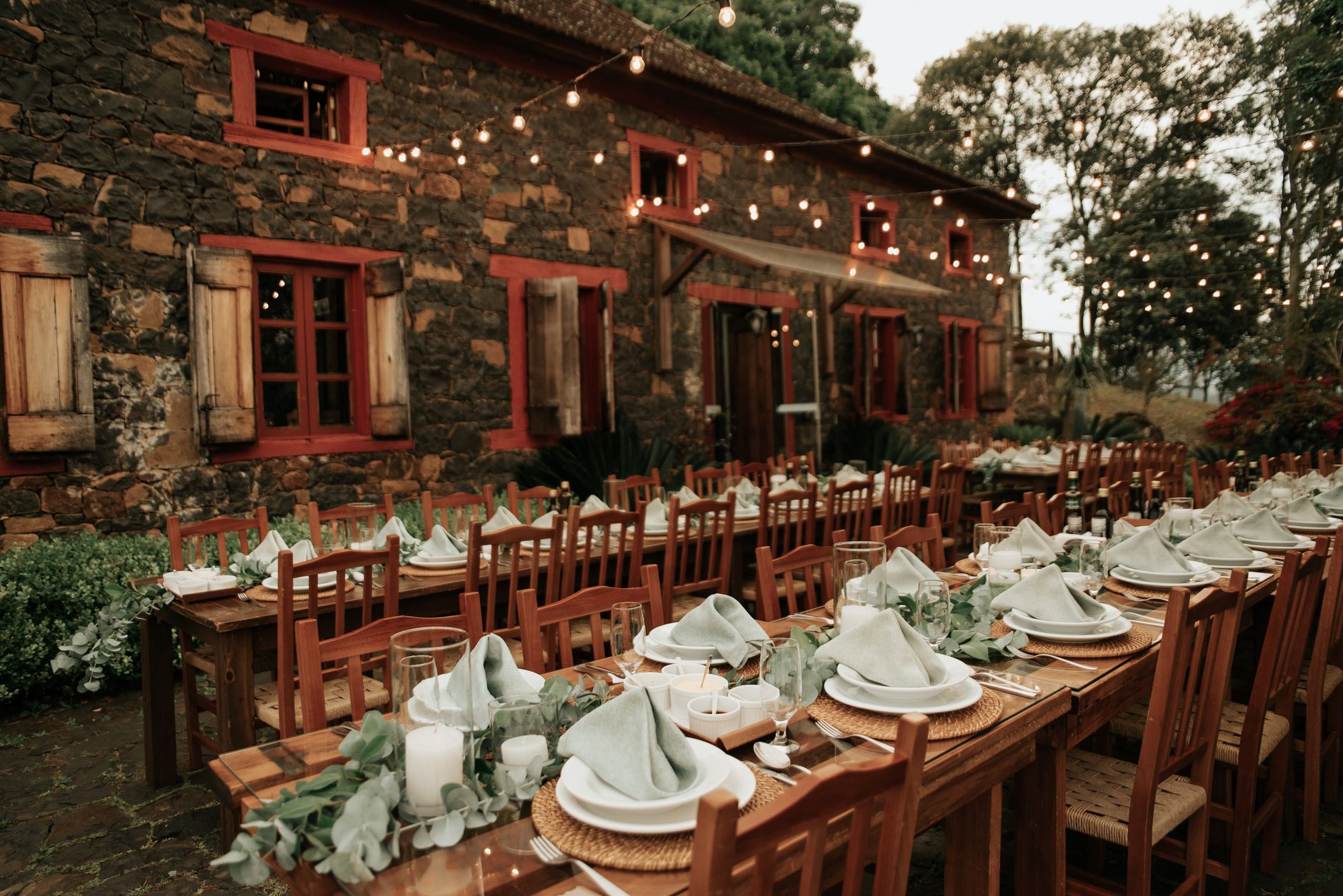 Outdoor rustic dinner setting with string lights, wooden tables, and stone building, creating a warm ambiance.