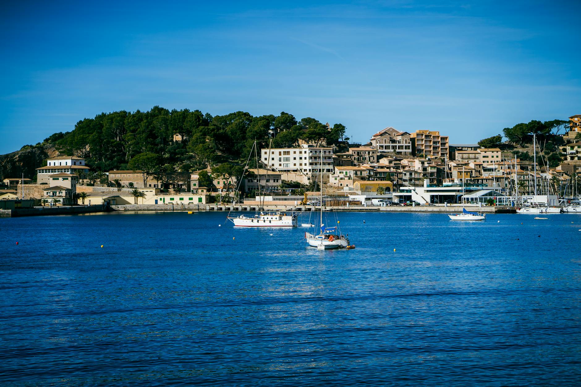 A tranquil coastal town with a marina, yachts, and hillside architecture in summer.