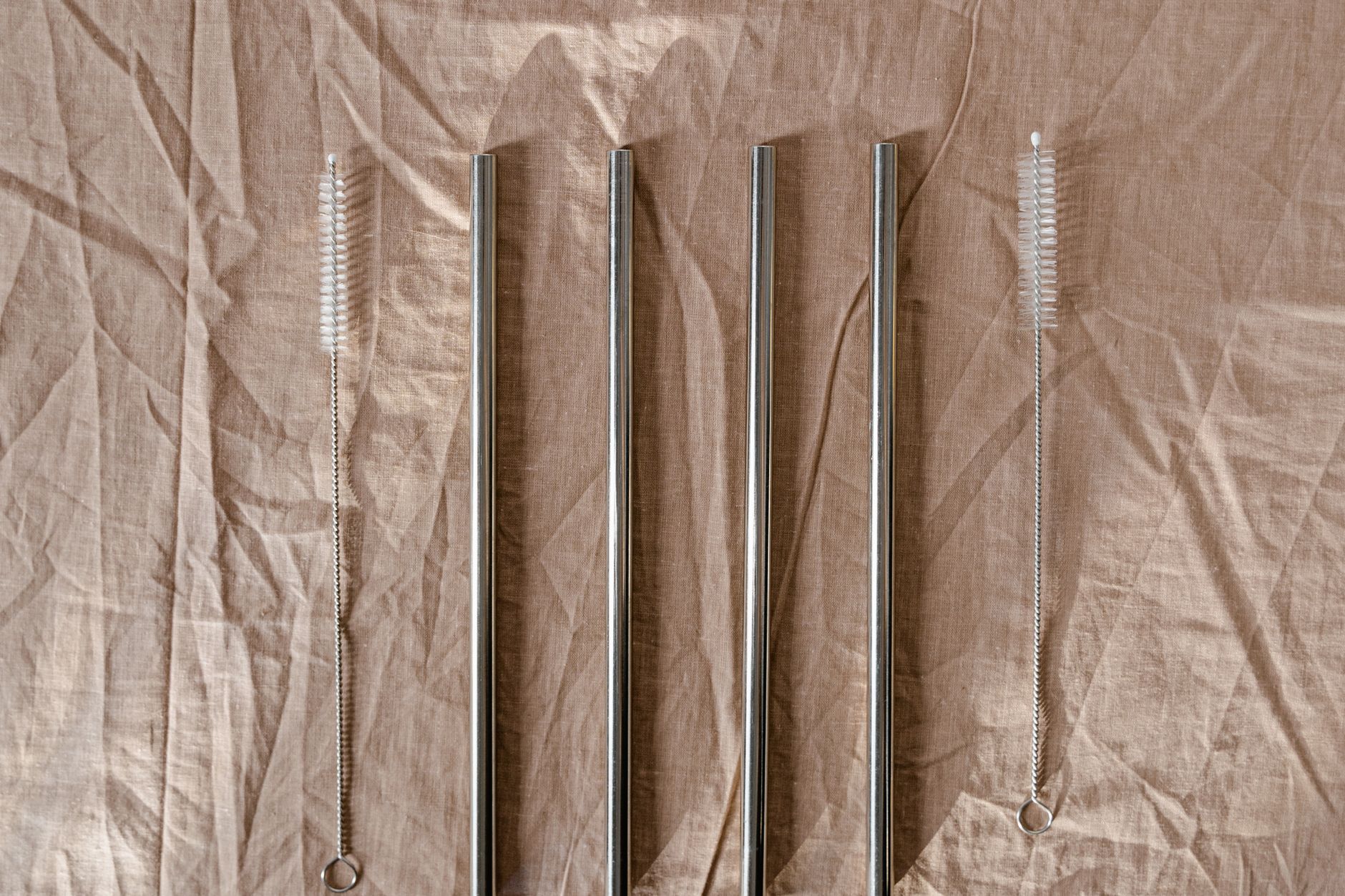Set of stainless steel straws with cleaning brushes on a textured brown background.