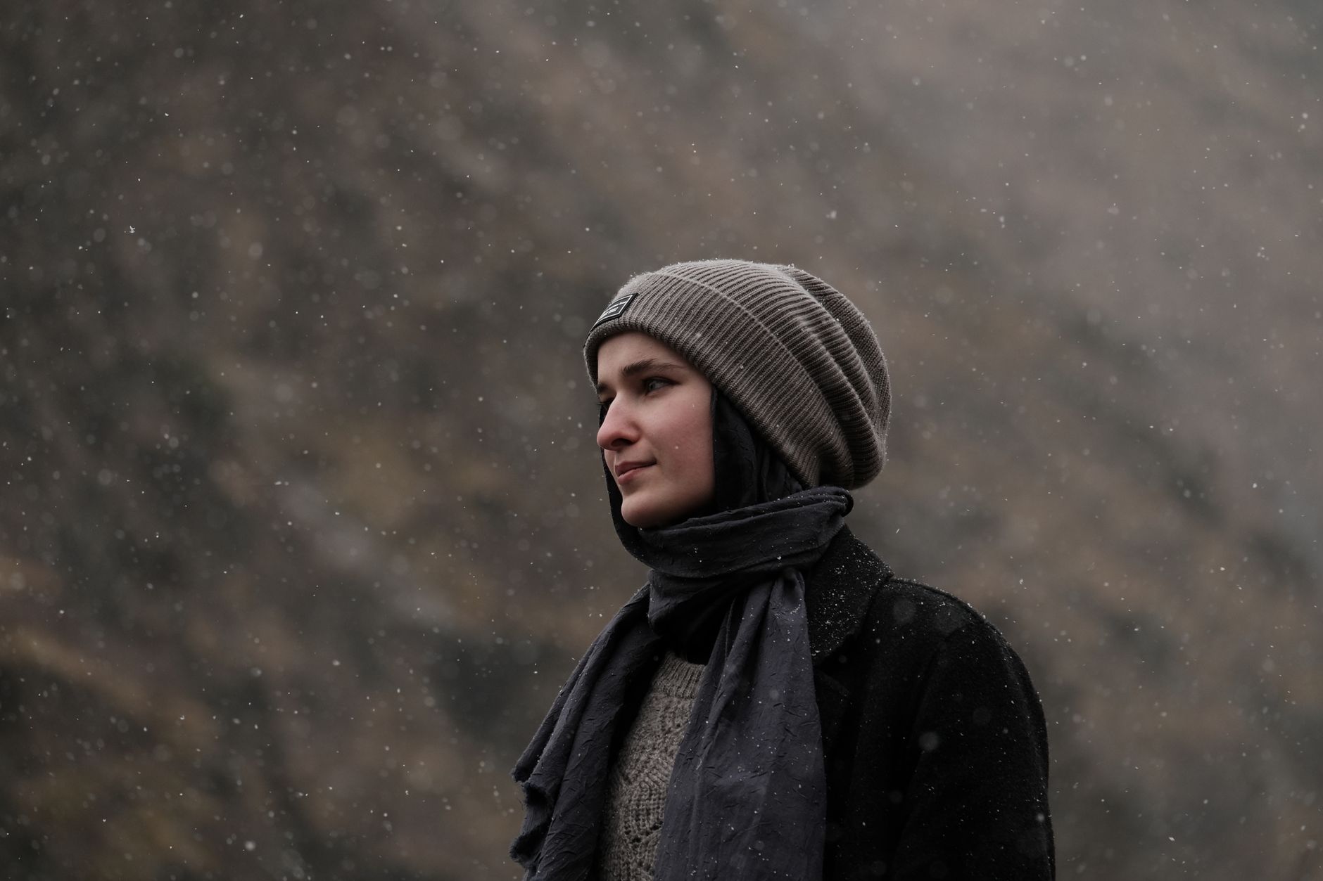 Portrait of a young woman in winter attire with knit hat and scarf under snowfall.