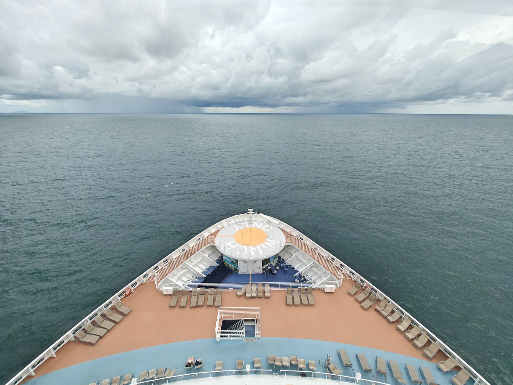 Empty cruise ship deck with deckchairs, calm ocean view, and dramatic clouds.