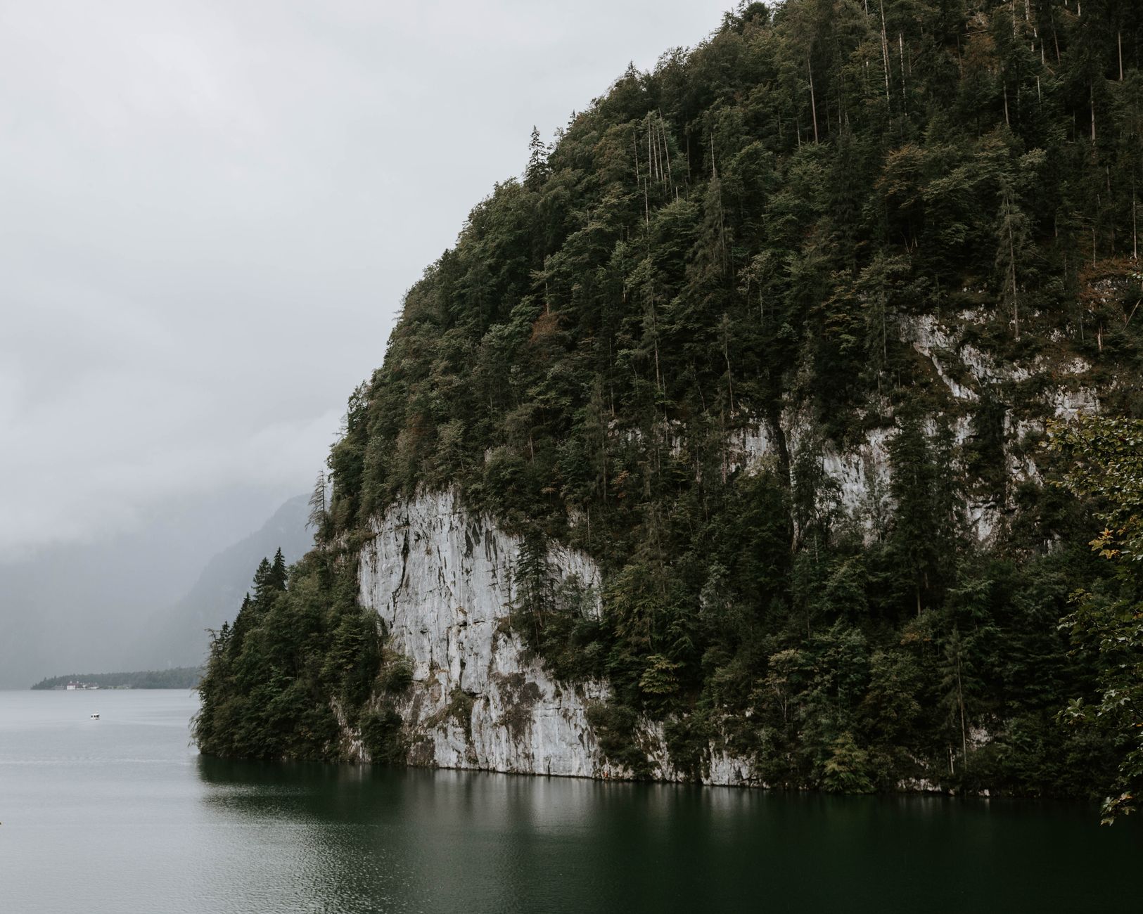 Misty morning view of serene lake surrounded by cliffs and forest in Schönau am Königssee, Germany.