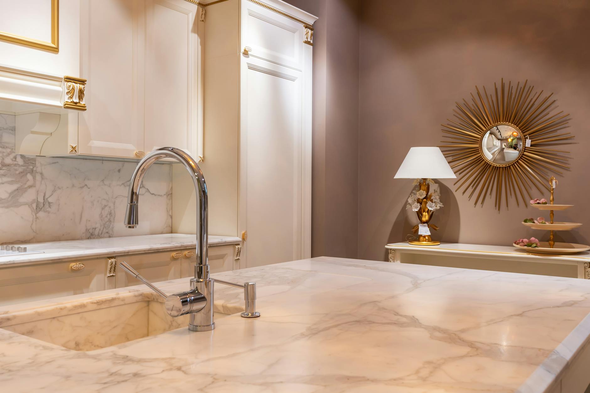 Sink with faucet on marble counter in modern stylish kitchen with white cabinets and glowing lamp near decorations in apartment