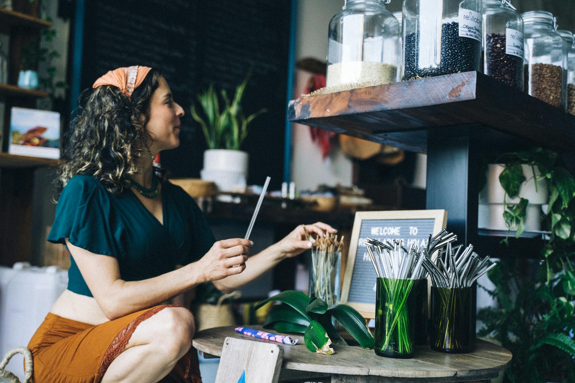 A woman crouches in a store choosing eco-friendly straws from a display.