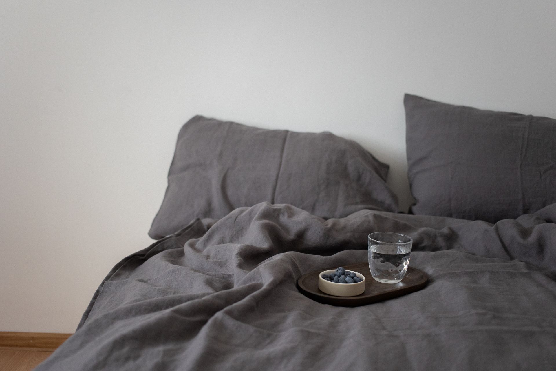 Ruhiges, helles Schlafzimmer mit naturfarbener Leinenbettwäsche in weichen Falten, gedämpftes Tageslicht, reduzierte Einrichtung