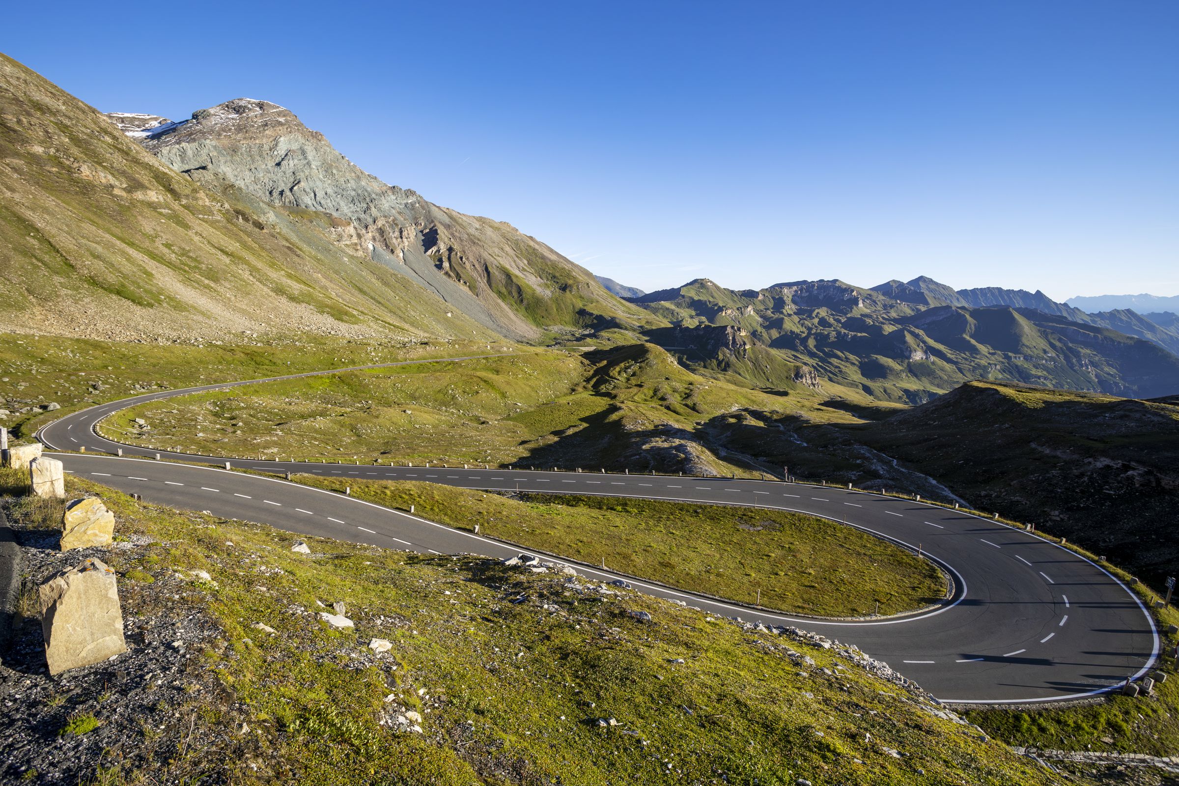A tight S-curve of the Stilfser-Joch-Straße with light stone markings along the edge of the road and green slopes under clear skies