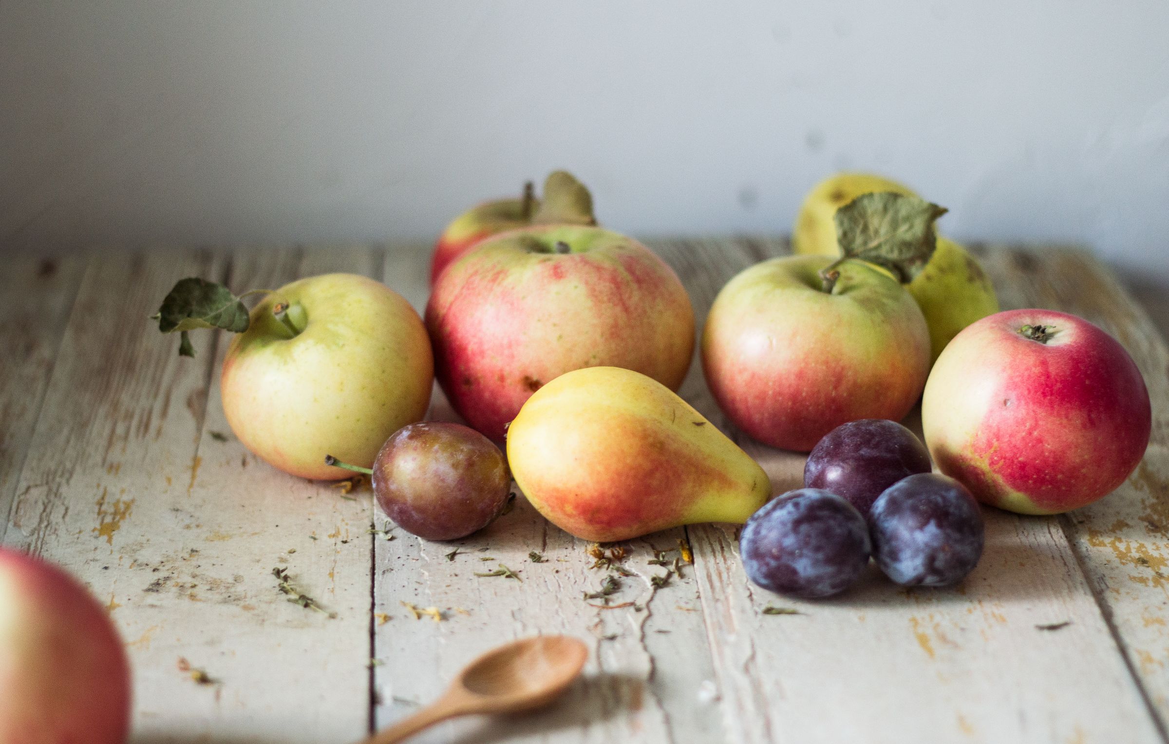 Still life of apples, pears, and plums on a weathered wooden table, some fruits with leaves.