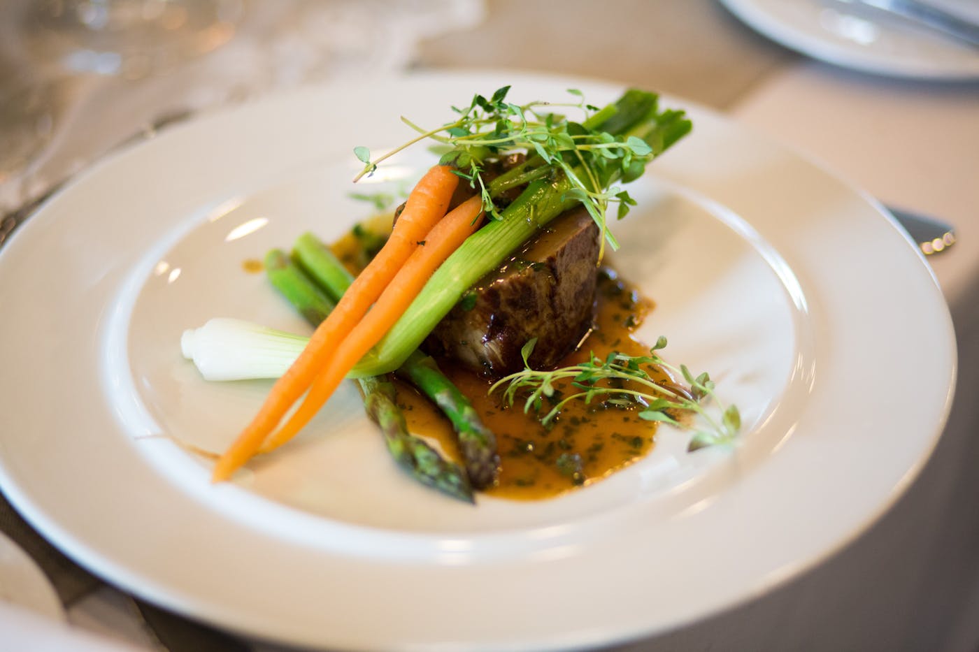 Fein angerichteter Gourmet-Teller mit Filet, Frühlingsgemüse und Jus auf weißem Porzellan
