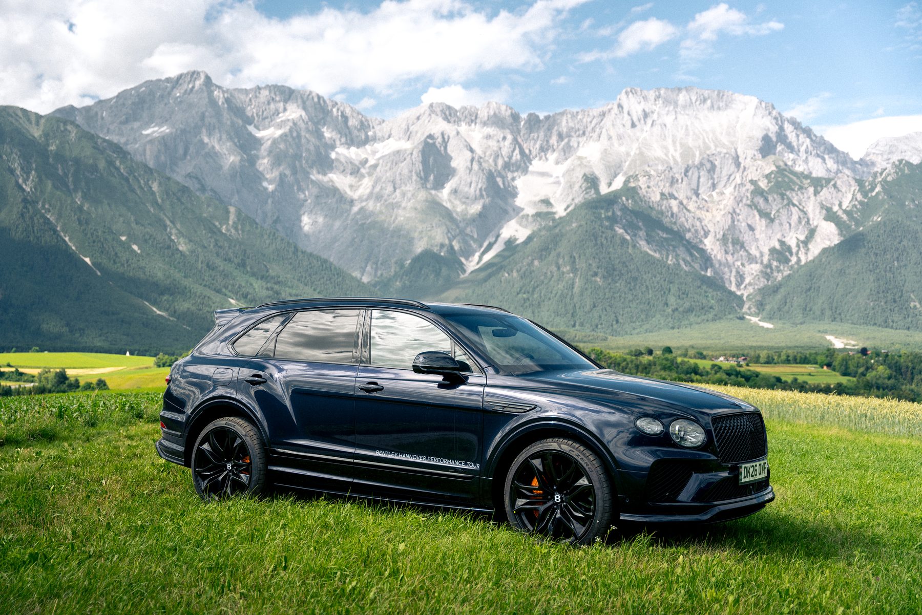 Dark-blue Bentley Bentayga on an alpine meadow with Tyrolean peaks in the background