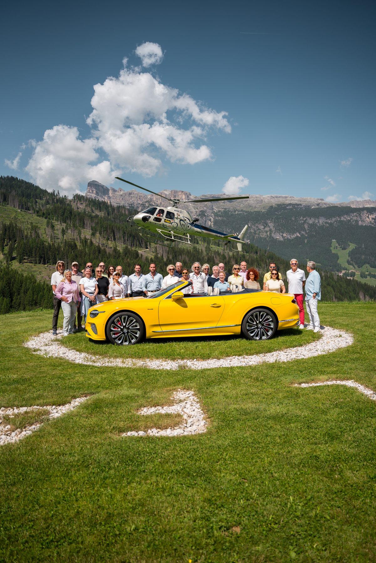 Group photo of participants in front of a yellow Bentley convertible and a helicopter