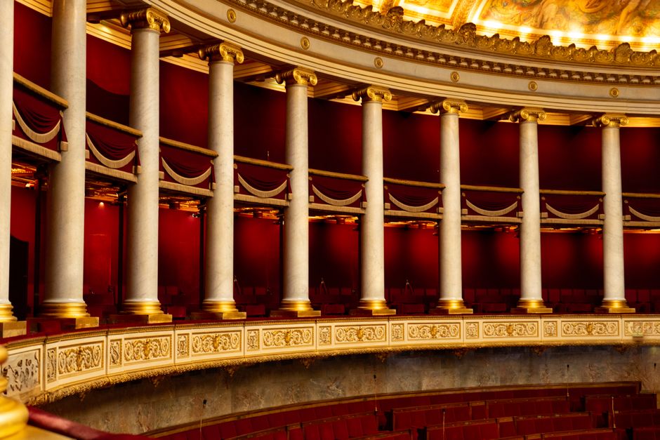 Geschwungener Rang mit Marmorsäulen und roter Drapierung in einem Opernhaus