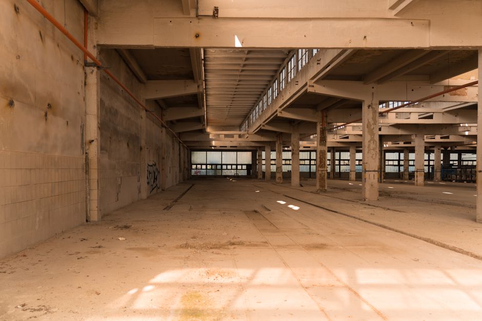 Wide empty industrial hall with concrete pillars and daylight streaming in