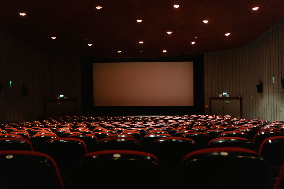 Klassischer Kinosaal mit heller Leinwand und roten Sitzreihen