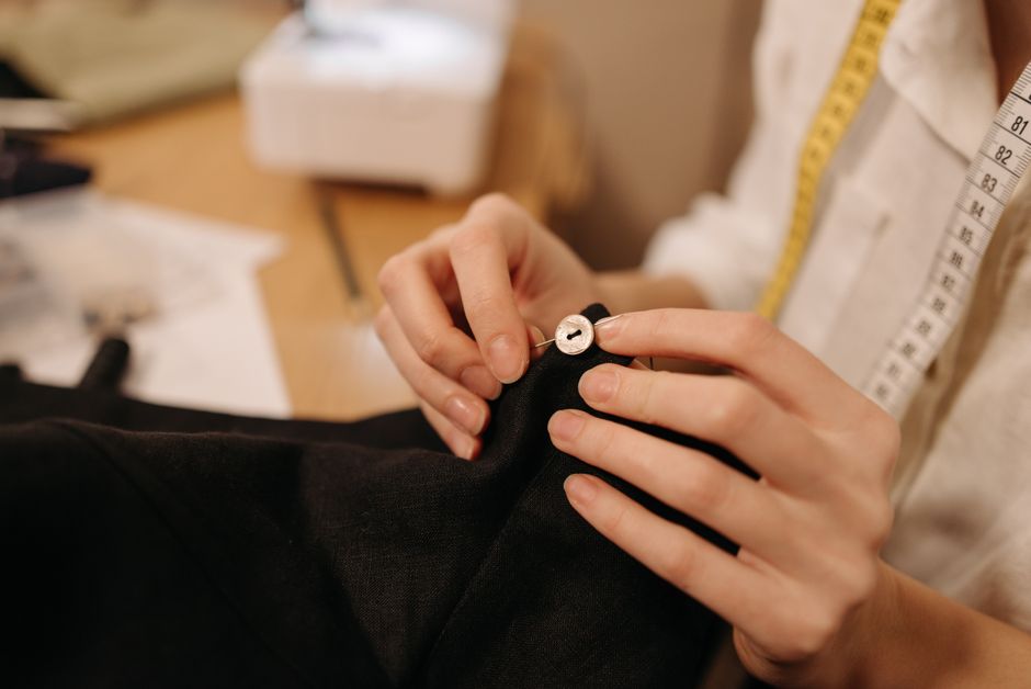 Hände nähen von Hand einen Knopf an dunklen Stoff im Atelier
